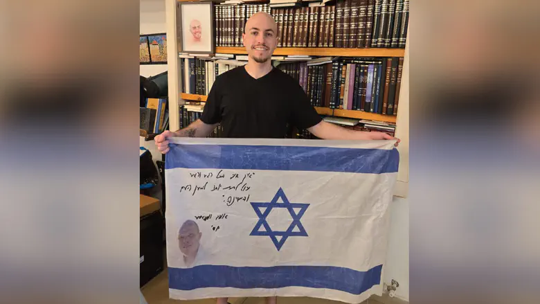 Hostage survivor Eitan Mor holds up Israeli flag of fallen soldier Yossi Hershkovitz