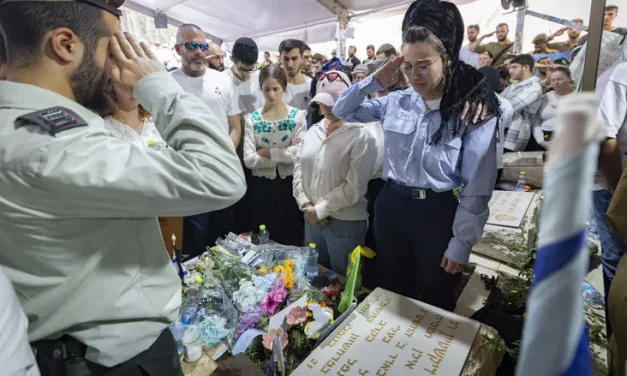 During the siren, Miriam Dickshtein salutes besides her fallen husband’s grave